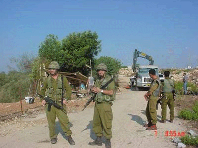 Four Israeli soldiers stand guard as the flower stand is demolished.