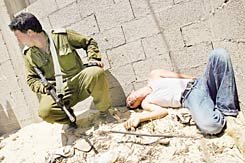 Palestinian boy who had been brutally beaten by settler youths lies against a wall; an Israeli soldier crouches near him.