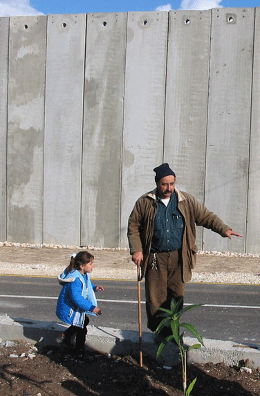 Hani and his daughter stand in the small area between their home and the Apartheid Wall built between them and their town, Mas’ha.