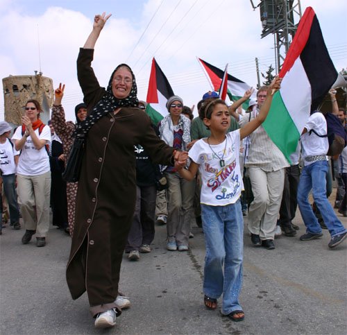 A smiling woman and child carrying a Palestinian flag lead the march.