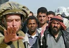 Israeli soldier signals to stop with his hand. Numerous Palestinians wait behind him