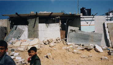 Photo of a Gaza Refugee Camp. Shacks surrounded by rubble are constructed from sheets of metal.